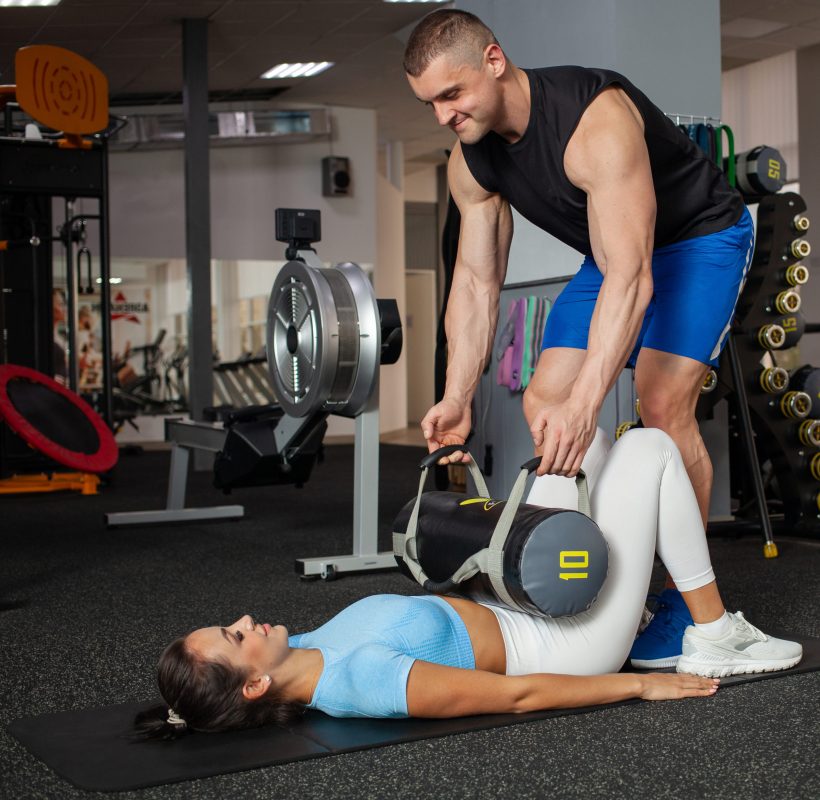 the trainer helps the woman to perform the exercise with a weighting agent. Sports body, fitness, weight loss, individual classes, coaching. Gym, healthy lifestyle. man and woman